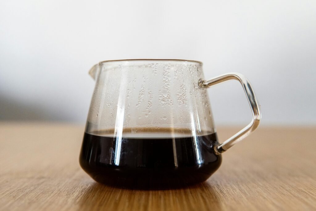 Um decanter de vidro transparente contendo café preto fresco sobre uma superfície de madeira.